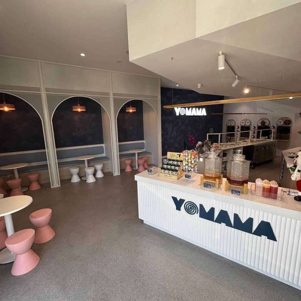 Modern café acai frozen yoghurt interior featuring stylish seating, a counter with colorful beverages, and the "YOMAMA" logo prominently displayed.